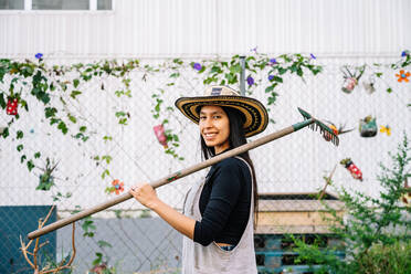 Happy young woman with rake standing in urban garden - GDBF00030