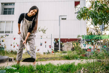 Glückliche junge Frau bei der Gartenarbeit mit Schaufel im städtischen Garten - GDBF00040