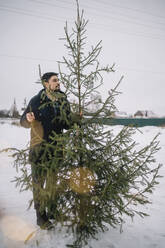 Man with fir tree standing in snow - ANAF00900