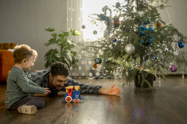 Glücklicher Vater und Sohn spielen zu Hause mit einer Spielzeugeisenbahn - ANAF00912