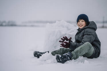 Glücklicher Junge mit Strickmütze, der mit einem Schneeklumpen spielt - ANAF00919