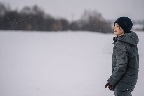 Lächelnder Junge mit Strickmütze im Schnee stehend - ANAF00920