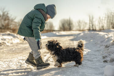 Happy boy playing with dog in snow - ANAF00923