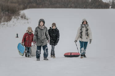 Happy family walking with inflatable sled in snow - ANAF00930