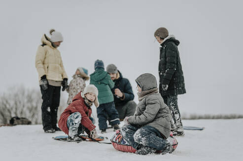 Glückliche Familie, die zusammen mit einem aufblasbaren Schlitten im Schnee Spaß hat - ANAF00934