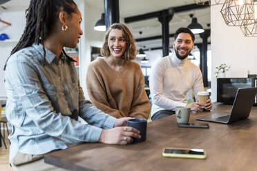 Lächelnde Geschäftsleute, die mit einer Tasse in einer Büro-Cafeteria sitzen - WPEF06963