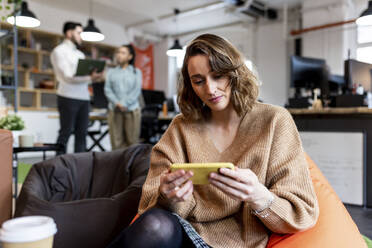 Businesswoman looking at smart phone sitting on bean bag in office - WPEF06983