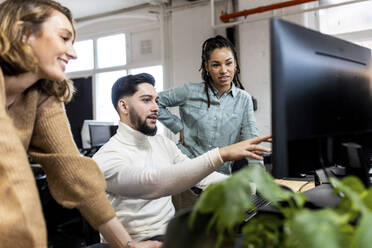 Junger Geschäftsmann erklärt Kollegen die Benutzung eines Desktop-PCs im Büro - WPEF06986