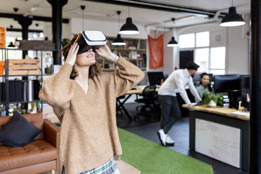 Businesswoman wearing virtual reality simulator standing in office - WPEF06991