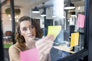 Businesswoman reading adhesive notes seen through glass - WPEF06996