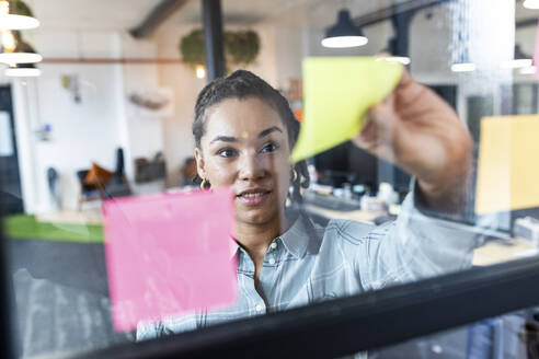 Businesswoman sticking adhesive notes on glass - WPEF06998