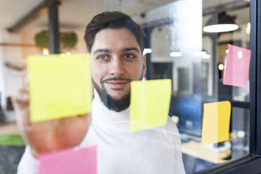 Smiling businessman sticking notes on glass - WPEF07000