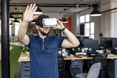 Young businessman wearing VR glasses gesturing at office - WPEF07046