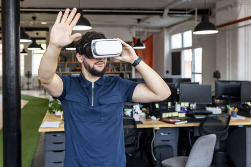 Junger Geschäftsmann mit VR-Brille gestikuliert im Büro - WPEF07046