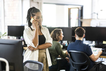 Lächelnde Geschäftsfrau, die im Büro mit einem Mobiltelefon spricht - WPEF07071