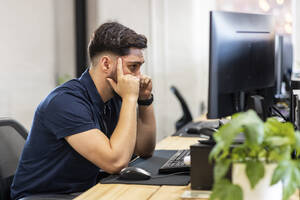 Frustrierter Geschäftsmann, der im Büro vor einem Desktop-PC sitzt - WPEF07075