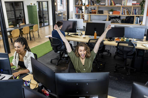 Happy businesswoman with arms raised working with colleagues in office - WPEF07084