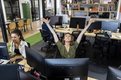 Glückliche Geschäftsleute mit erhobenen Armen bei der Arbeit im Büro - WPEF07085