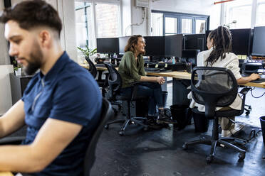 Businesswoman having discussion sitting at desk in office - WPEF07086