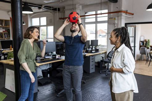 Glückliche Geschäftsleute, die im Büro mit einem Ball spielen - WPEF07089