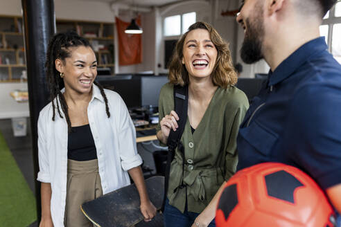 Happy business colleagues with skateboard and ball standing in office - WPEF07092