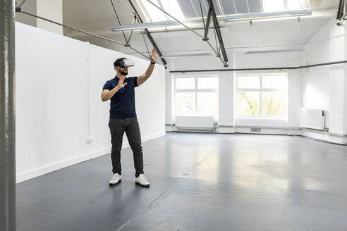 Businessman wearing virtual reality glasses gesturing in office - WPEF07102