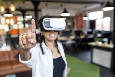 Businesswoman wearing VR glasses pointing in office - WPEF07118