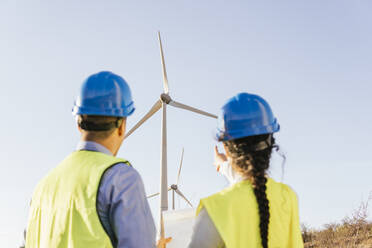 Engineer with colleague gesturing and discussing over wind turbines - MGRF00860