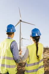 Engineers discussing over wind turbines on sunny day - MGRF00861