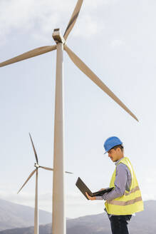 Ingenieur arbeitet an einem Laptop vor einer Windkraftanlage - MGRF00875