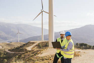 Techniker und Ingenieur arbeiten an einem Laptop vor einer Windkraftanlage - MGRF00877