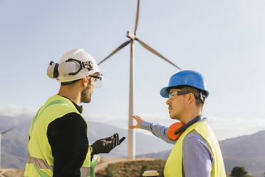 Technician and engineer discussing over wind turbine on sunny day - MGRF00878