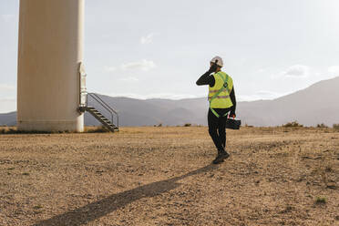 Technician with toolbox walking towards wind turbine - MGRF00880