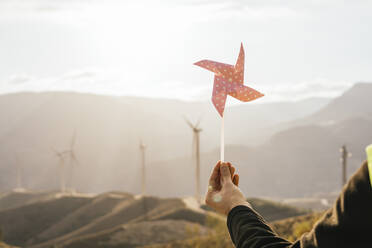 Die Hand eines Technikers hält ein Windrad vor einer Windkraftanlage - MGRF00884