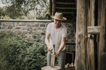 Man wearing hat chopping firewood with axe - MJRF00865