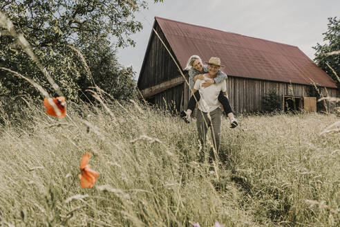 Senior man piggybacking woman in field - MJRF00880