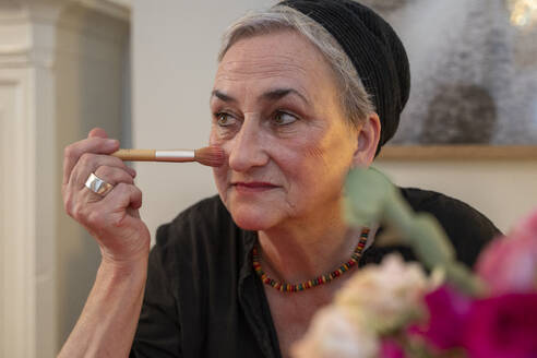 Senior woman applying make-up with brush at home - NGF00784