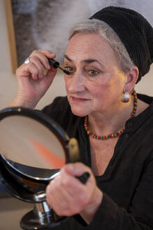 Woman in skullcap applying mascara at home - NGF00785