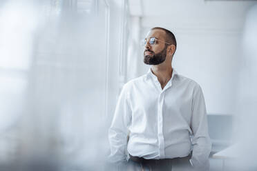 Thoughtful businessman wearing eyeglasses standing at home office - JOSEF15950