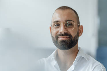 Smiling businessman wearing eyeglasses in front of wall - JOSEF15988