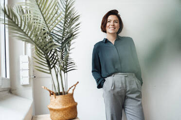 Thoughtful businesswoman standing with hands in pockets at office - JOSEF16037