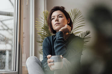Nachdenkliche Geschäftsfrau mit Kaffeetasse am Fenster sitzend - JOSEF16041