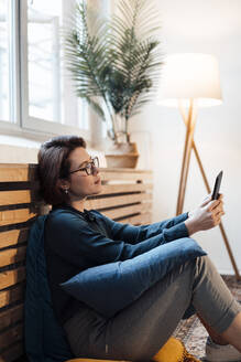 Businesswoman with tablet PC sitting in front of heating radiator - JOSEF16048