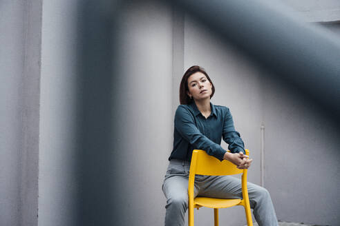 Junge Geschäftsfrau sitzt auf einem Stuhl vor einer Wand - JOSEF16064