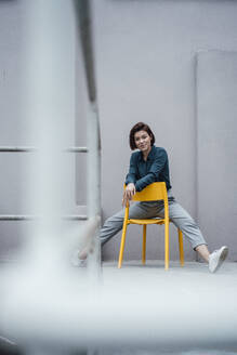 Junge Geschäftsfrau sitzt auf einem Stuhl vor einer grauen Wand - JOSEF16067