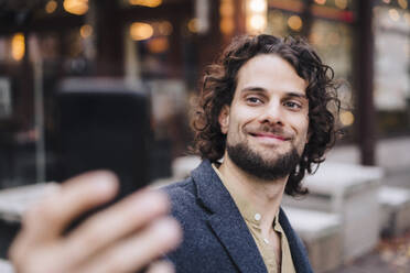 Lächelnder junger Geschäftsmann, der ein Selfie vor einem Cafe macht - JOSEF16109