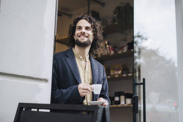 Lächelnder junger Geschäftsmann mit Kaffeetasse am Eingang - JOSEF16113
