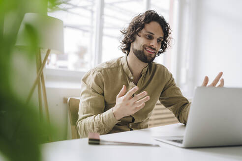 Lächelnder junger Geschäftsmann bei einem Videoanruf über einen Laptop am Arbeitsplatz - JOSEF16153