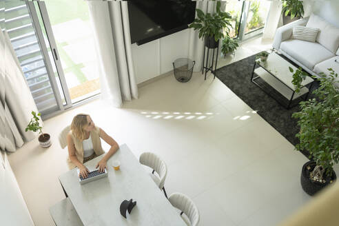 Freiberufler mit Laptop sitzt am Tisch im Wohnzimmer zu Hause - SVKF01092