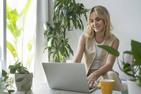 Smiling freelancer working on laptop at home office - SVKF01093